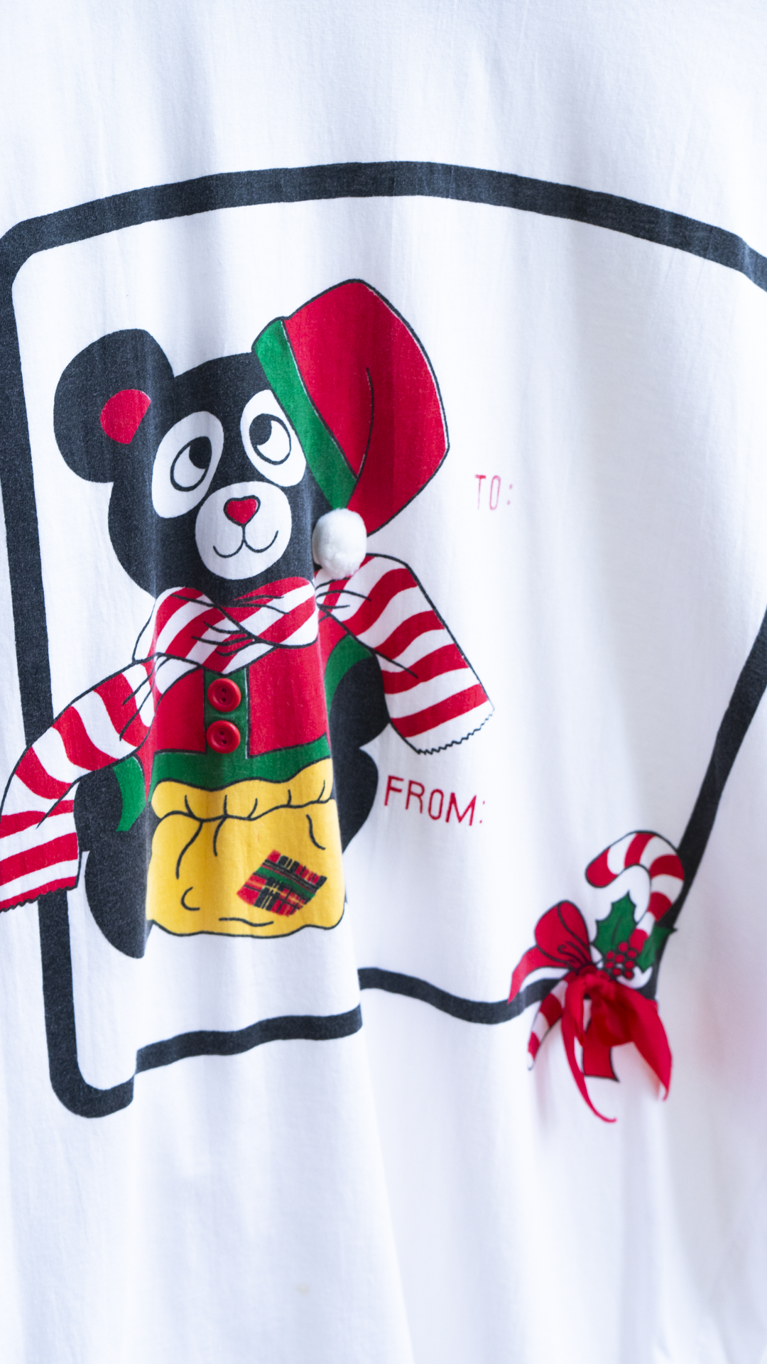 close up of a teddy bear on a white and red 80s christmas nightshirt with a DIY card showing the text 'TO:' and 'FROM:' and a candy cane.