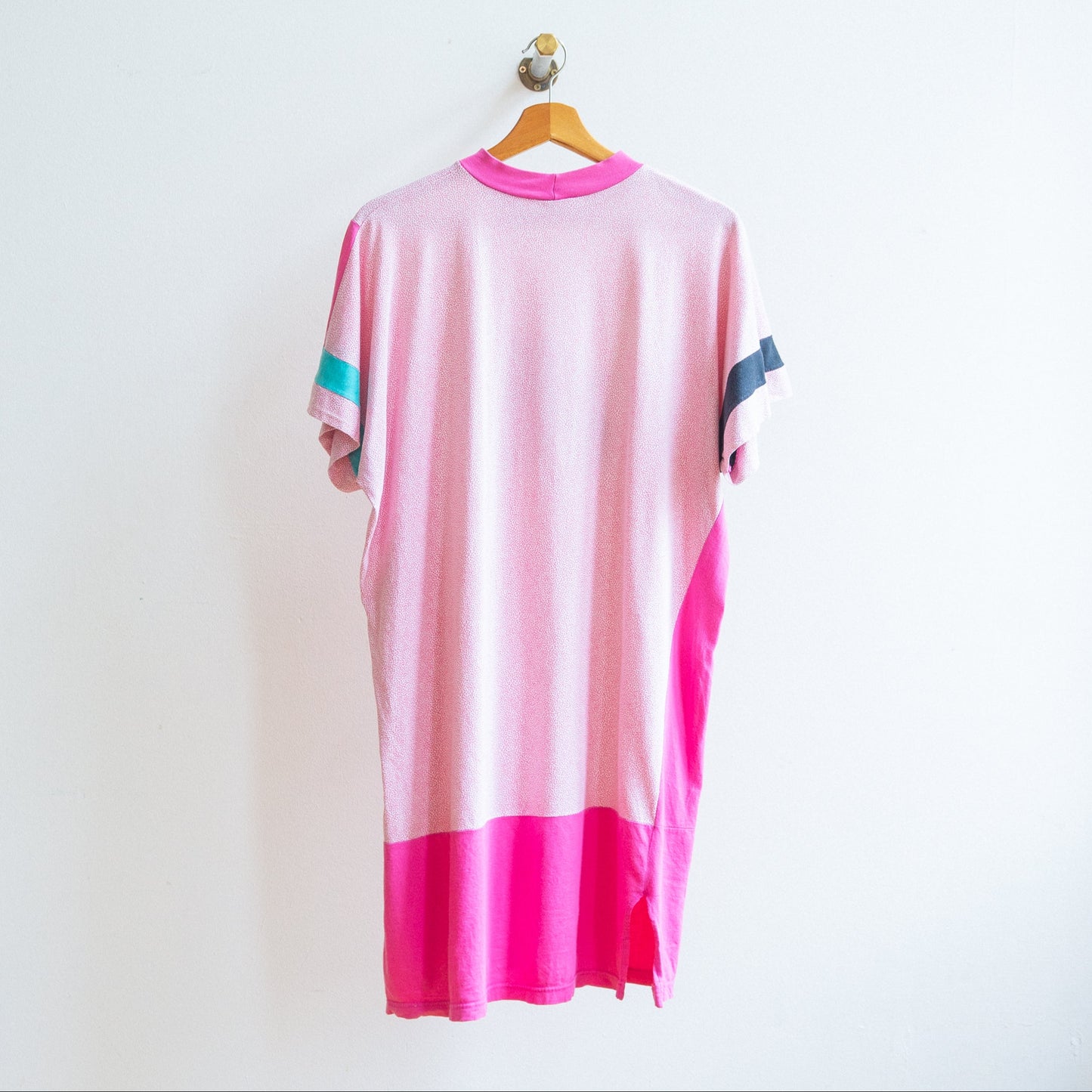Back of a pink and white oversized t-shirt or dress from the 80s with short sleeves on which are asymmetrical color accents in teal and black