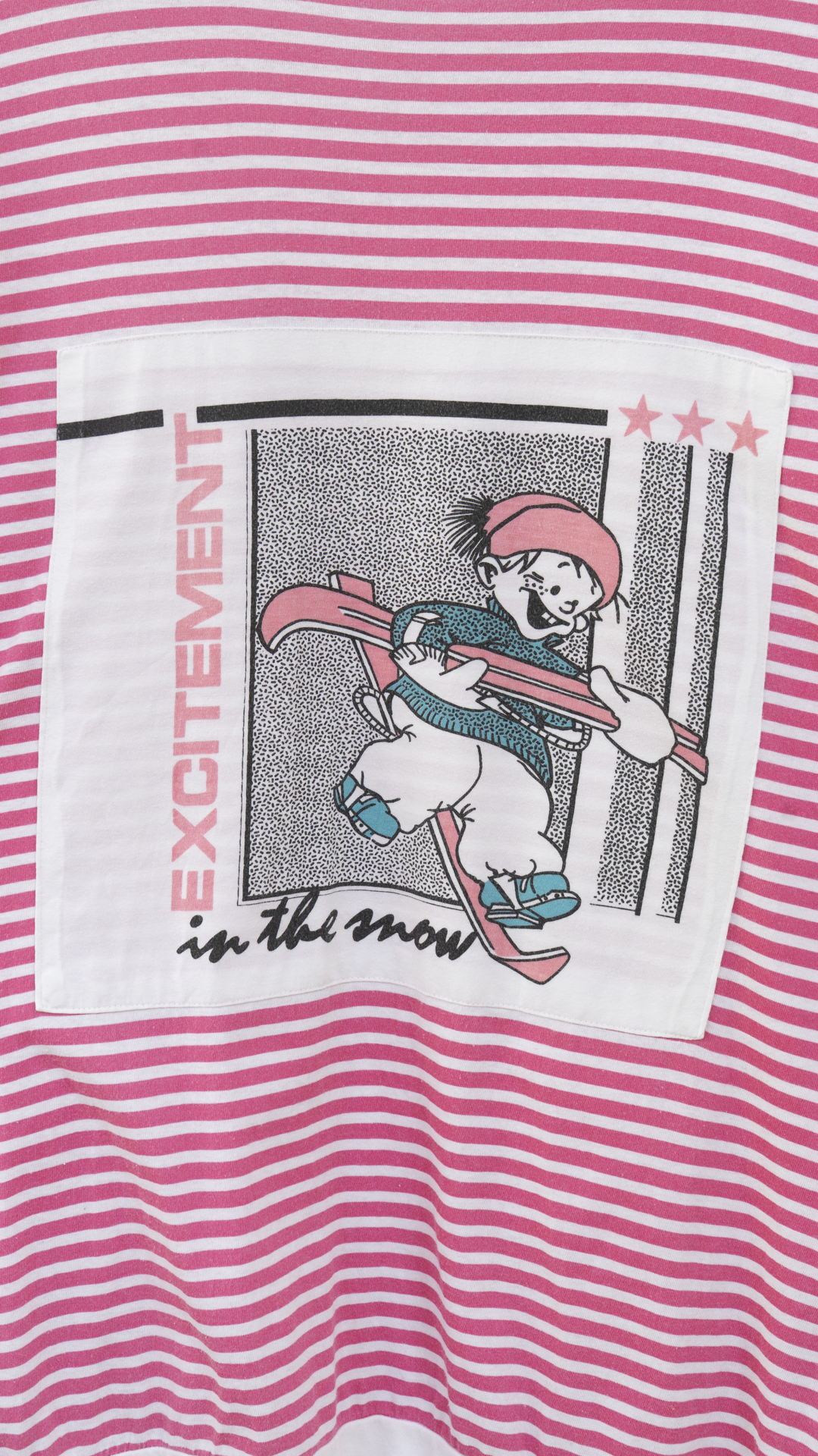 zoom-in print of a child with skis and the text 'excitement in the snow' of a pink white striped 80s oversized sleep t-shirt