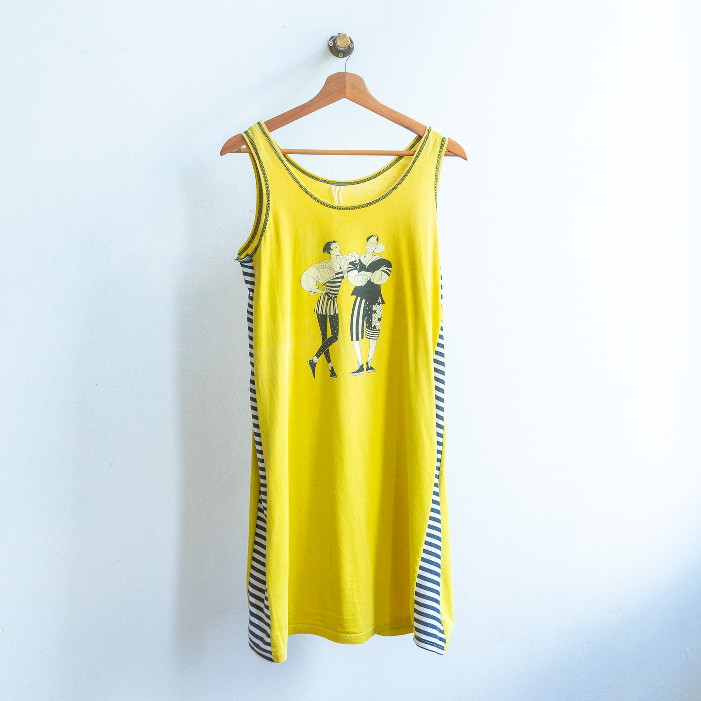 Yellow secondhand sleeveless dress  with black and white graphic on a hanger against a white wall.