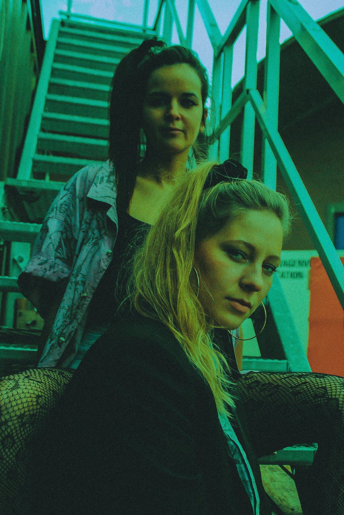 twee vrouwen die jaren 80 vintage kleding dragen zitten samen op een metalen trap