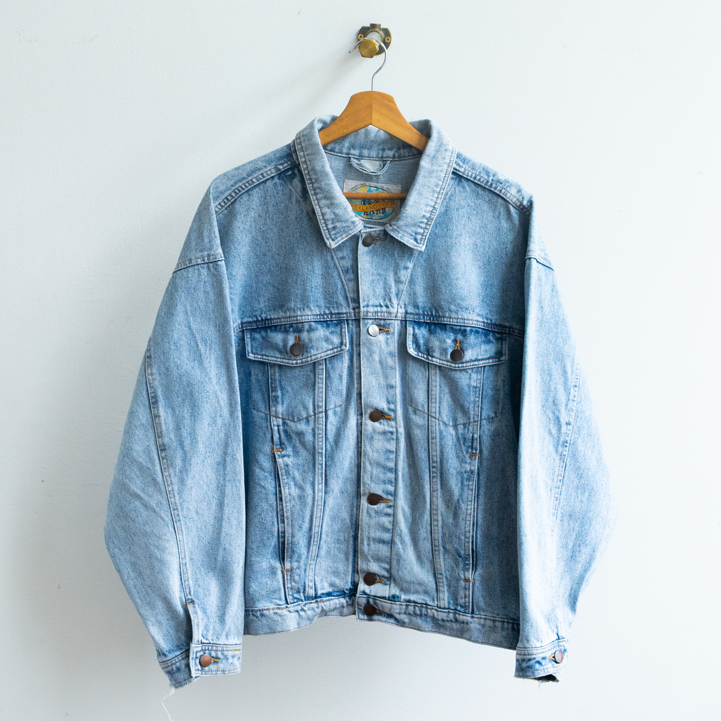 A light wash vintage 90s blue denim jacket hanging on a wooden hanger against a plain white wall