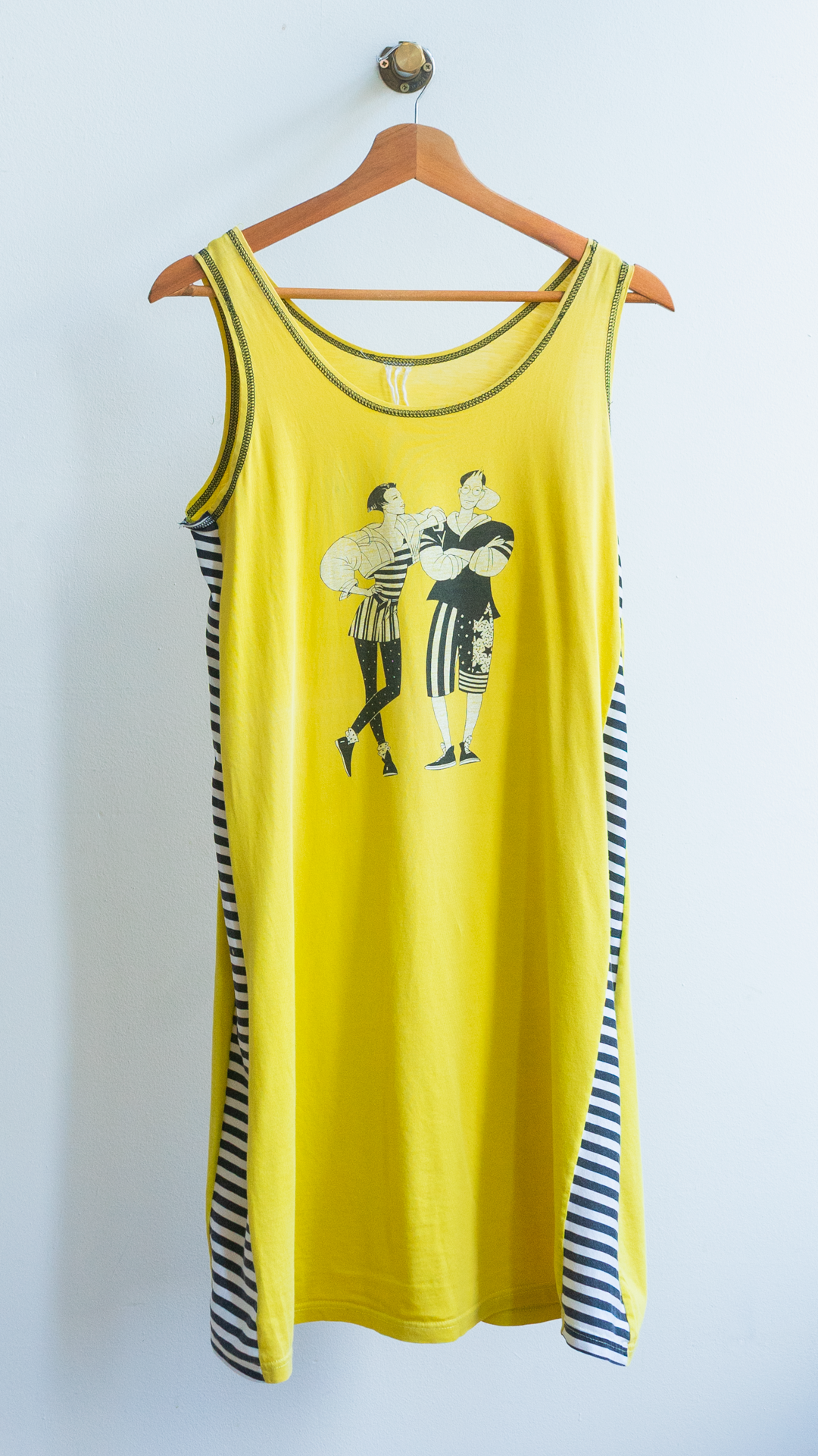 Yellow secondhand sleeveless dress  with black and white graphic on a hanger against a white wall