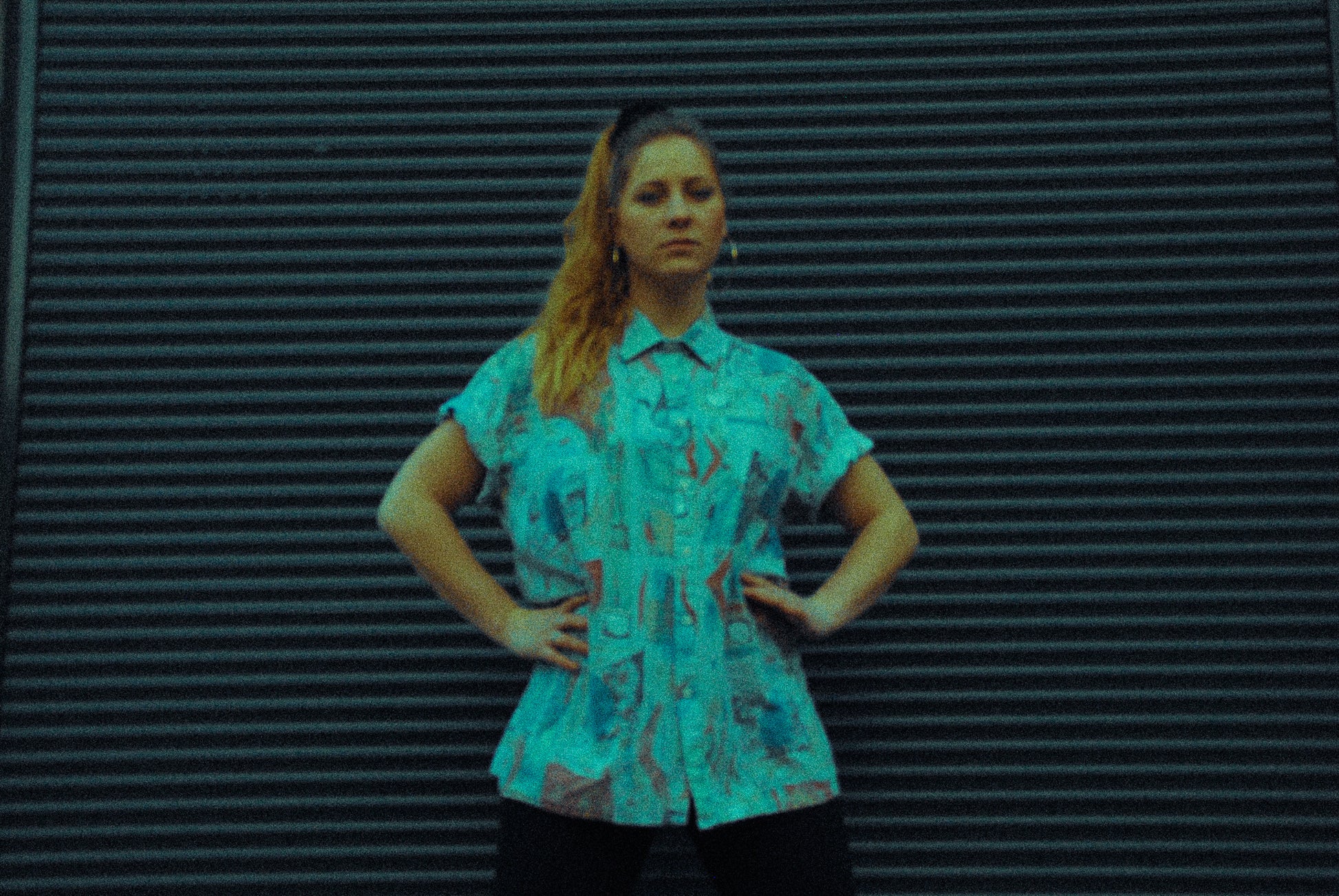 artsy picture of a young woman in front of a garage door wearing an abstract shirt and big round earrings 90s classy ghetto style 